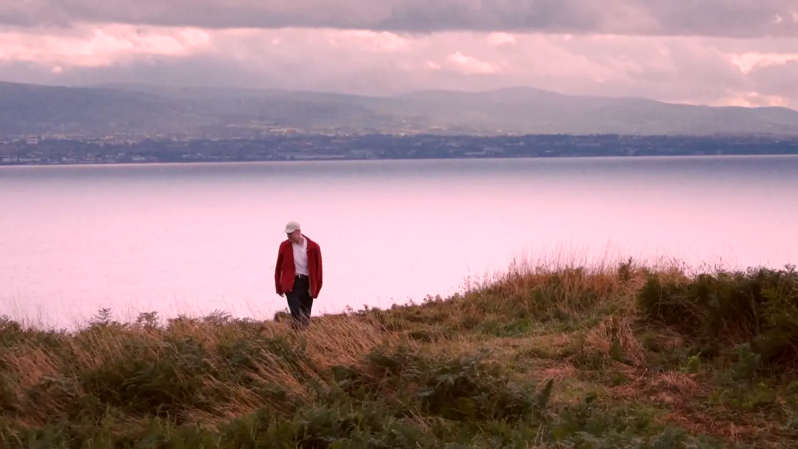 Walshy standing in long grass above the sea at dusk, from one of his music videos